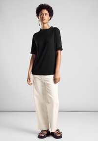 Haut noir à manches courtes côtelé avec un col rond et un détail de bouton sur une épaule, associé à un pantalon crème à jambes larges et des sandales marron.