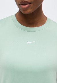 Κοντινό πλάνο ενός ατόμου που φοράει ανοιχτοπράσινο μπλουζάκι Nike με λευκό λογότυπο Nike swoosh στο κέντρο κοντά στον γιακά.