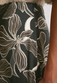 Jupe à motif floral en vert foncé, avec des fleurs blanches et beige. Fermeture éclair sur le côté, tissu léger avec une texture lisse.
