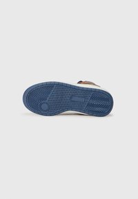 Sola de sapato com um fundo de borracha azul apresentando padrões em zigue-zague e um ponto de aderência circular, contrastando com a parte superior castanha.