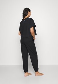 T-shirt noir en coton cropped à manches courtes avec le logo Calvin Klein au dos, associé à un pantalon de jogging noir avec des poignets élastiques.