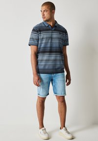 Pruhované polo tričko v námořnické modři a světle modré, s designem krátkých rukávů. V kombinaci se světle modrými džínovými šortkami a bílými teniskami.