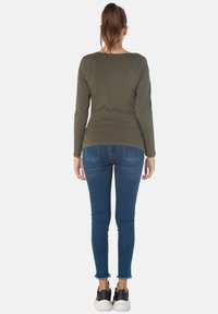 Olivenfarbener Langarmtop mit rundem Ausschnitt, kombiniert mit dunkelblauen Skinny Jeans mit ausgefransten Säumen und schwarzen Turnschuhen.