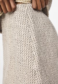 Bežová tkanina se vzorem, který vyniká texturou. Detailní pohled zvýrazňuje odlišné tkaní s jemnými černými akcenty a bezespárným zakončením.