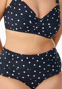 Svart bikini med prickar, som har en snodd framtill på toppen och höga midjebyxor med rynkning på sidorna för en samlad effekt.