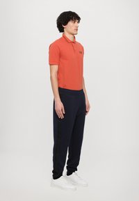 Herre orange polo skjorte med krave, sammen med marineblå sweatpants med en lodret struktureret stribe og hvide sneakers.