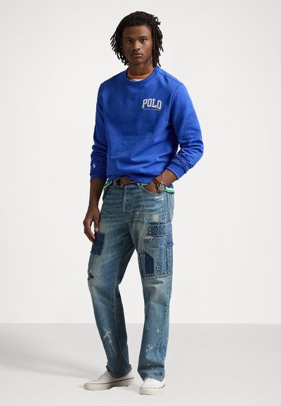 Zils kokvilnas džemperis ar "Polo Ralph Lauren" logo, saskaņots ar kaprīzajiem denima cargo biksēm ar dažādiem zila toņiem un nolietojumiem.