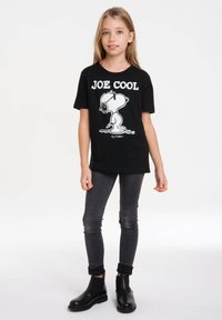 Black cotton t-shirt featuring a white graphic of Snoopy with "JOE COOL" text. Paired with dark jeans and black ankle boots.