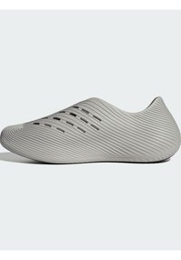 Ανοιχτό γκρι παπούτσι με κομψό, λείο σχεδιασμό που διαθέτει κυματιστές ραβδώσεις και ανοίγματα για αερισμό. Στρογγυλερή μύτη και σταθερή σόλα.