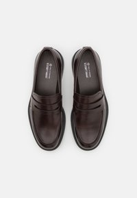 Mocasines de cuero vegano marrón con un acabado suave, acentos de tiras paralelas dobles y una plantilla acolchada. Suela de goma con patrón de tracción.