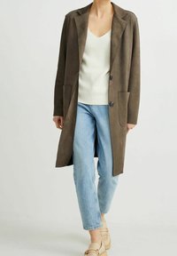 Abrigo largo de ante marrón con solapa, dos bolsillos frontales y dos botones. Combinado con una camiseta blanca de canalé y jeans azul claros.