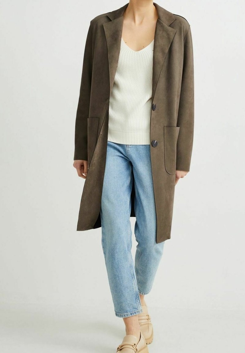 Abrigo largo de ante marrón con solapa, dos bolsillos frontales y dos botones. Combinado con una camiseta blanca de canalé y jeans azul claros.
