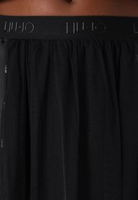 Jupe en tulle noir avec une large ceinture élastique présentant le logo "LIU JO" en relief dans un noir brillant.