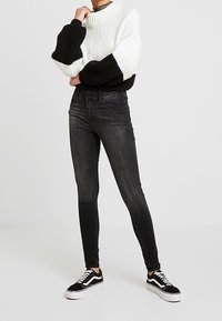 Suéter de punto con diseño en bloques de color negro y blanco, cuello alto y mangas extragrandes. Jeans negros ajustados combinados con zapatillas negras.