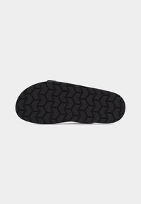 Semelle de chaussure noire avec un motif de bande de roulement en zigzag profond conçu pour l'adhérence et la durabilité, isolée sur un fond blanc.