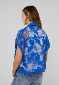 Blue lace kimono-style jacket with floral pattern and open weave design. Features a collar and relaxed fit with short sleeves.