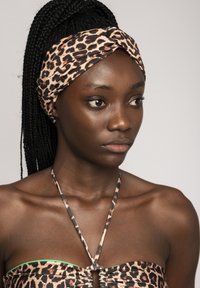Fascia per capelli in stampa leopardata nei toni del rosa e marrone, design attorcigliato, indossata con un top bikini a fantasia simile con un accento verde.