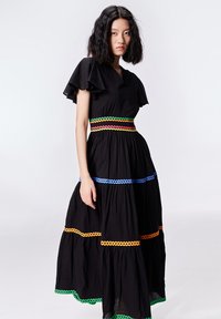 Robe maxi noire avec des petites manches volantées et une bordure en zigzag colorée en vert, orange, rose et bleu au niveau de la taille et de l'ourlet.