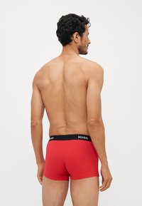 Caleçons boxers rouges en tissu doux avec une ceinture noire "HUGO", offrant une coupe ajustée et une texture lisse. Vue arrière montrée.