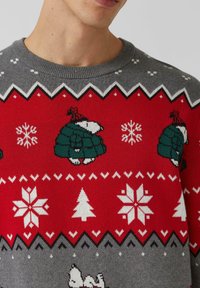 Szary i czerwony sweter robiony na drutach z wzorami igloo i płatków śniegu w kolorach zielonym i białym, z zygzakowatymi wzorami przy dekolcie i w talii.