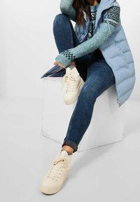 Veste matelassée bleu clair, pull à motifs en sarcelle et noir, jean skinny foncé, et baskets montantes crème à surface texturée.