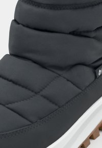 Botină neagră căptușită cu o textură matlasată, având o talpă albă și un profil de cauciuc maro. Materialul superior este neted și rezistent la apă.