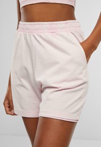 Shorts en coton rose clair avec une taille élastique et des poches latérales, offrant une coupe décontractée et des coutures nettes. Texture douce.