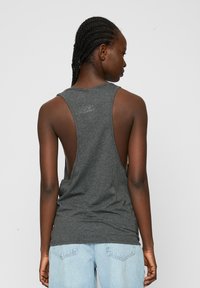 Grå ærmeløs tank top med et løst rygdesign, lavet af blødt stof. Matchende med lyseblå jeans, der viser en afslappet stil.