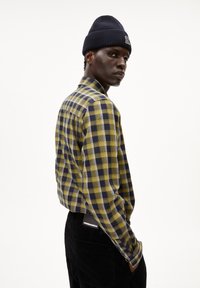 Geruite shirt in geel, groen en marineblauw; lange mouwen met knoopmanchetten. Gecombineerd met zwarte corduroy broek met een logo-label.