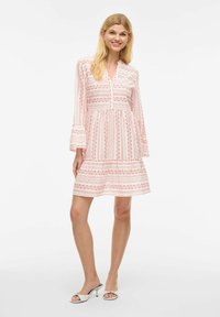 Robe blanche avec des motifs géométriques roses, un col boutonné et des manches évasées. Tissu lisse avec une silhouette fluide en A.
