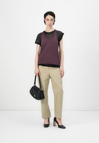 Donkerpaarse tanktop over een zwarte doorschijnende blouse, gecombineerd met lichtbeige broek. Zwarte handtas met gouden hardware en zwarte hoge hakken.