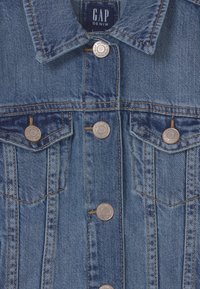 Kurtka dżinsowa w średnim niebieskim kolorze, z miedzianymi guzikami, klasycznym kołnierzem, dwoma kieszeniami na piersi oraz widocznymi przeszyciami.