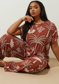 Set da salotto marrone con stampa di palme bianche, maniche corte e vestibilità comoda. Il tessuto presenta un aspetto testurizzato e rigato.