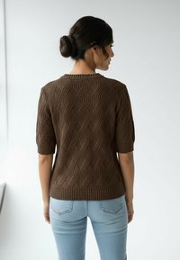 Brązowy dziany sweter z teksturowanym wzorem warkocza, krótkimi rękawami i prążkowanym kołnierzem, zestawiony z jasnoniebieskimi dżinsami.