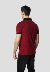 Punane polo-särk tekstuurse mustriga, musta krae ja mansettidega. Lühikeste varrukatega ja sirge äärega, kantud tumedate teksadega.