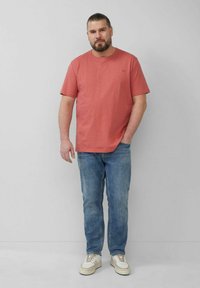 Rotes Baumwoll-T-Shirt mit kurzen Ärmeln, kombiniert mit hellblauen Jeans und weißen Sneakers, im lässigen Schnitt und mit Rundhalsausschnitt.