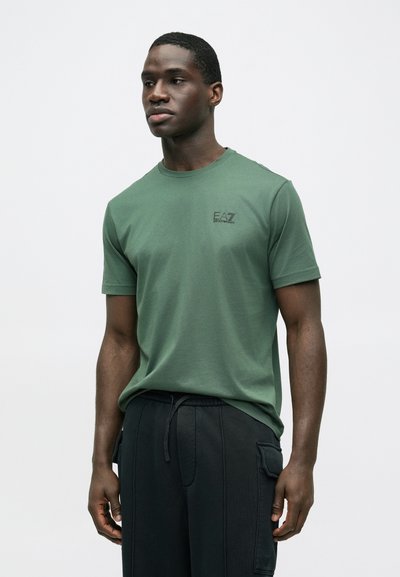 Zelené tričko s krátkym rukávom z mäkkého materiálu, s okrúhlym výstrihom a malým čiernym logom na ľavej strane hrudníka. Voľný strih na bežné nosenie.