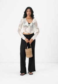 Gehaakte crop top met bloemmotief in het wit, gecombineerd met zwarte wijde broek. Geaccessoireerd met een ronde geweven tas en platte sandalen.