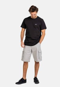 Schwarzes Baumwoll-T-Shirt mit kleinem Logo auf der Brust, kombiniert mit hellgrauen Cargo-Shorts mit seitlichen Taschen. Schwarze Sneakers runden den Look ab.
