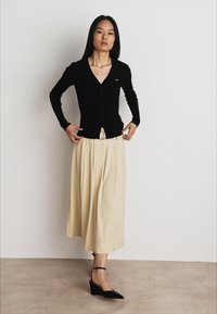 Melna pieguļoša kardigāna jaka ar pogu priekšpusi, savienota ar krēmveida plisētu midi svārku. Modelis valkā melnus platformu zābakus ar potīšu siksnām. Minimālistisks dizains.