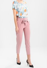 Short-sleeve blouse with floral pattern in blue, orange, and green; paired with pink tailored trousers featuring a tied waist detail.