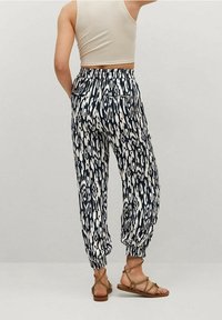 Pantalons de jogging à motifs bleu marine et blancs avec taille élastique, chevilles resserrées et deux poches arrière. Portés avec des sandales à lanières beiges.