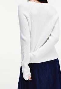 Pull en tricot blanc à texture côtelée, avec des manches longues et une coupe décontractée. Associé à une jupe bleu foncé texturée.