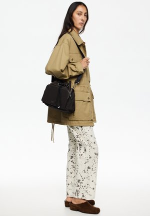 Khaki kurtka o oversize'owym kroju, kremowo-szare spodnie o szerokich nogawkach w wzór, brązowe zamszowe klapki oraz mała czarna torebka na ramię z zamkiem.