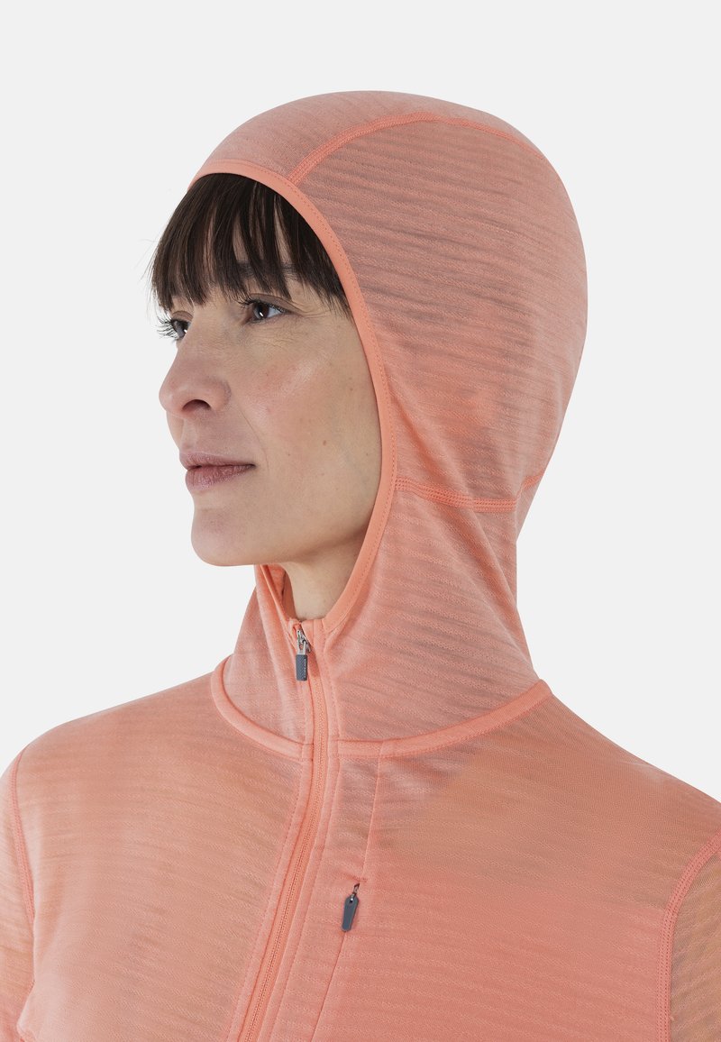 Veste légère à capuche en tissu corail doux, dotée d'une fermeture zippée et d'un motif texturé, conçue pour le confort et la mobilité.