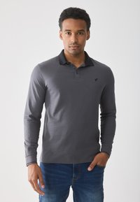 Long-sleeve polo shirt in dark gray cotton with a black collar, three-button placket, and a small logo on the chest. Worn with blue jeans.