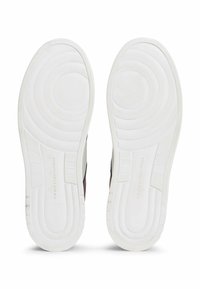 Brązowe sneakersy z białymi gumowymi podeszwami, posiadające teksturowane wzory grip i wytłoczone logo marki. Elegancki, minimalistyczny design bez widocznych elementów metalowych.