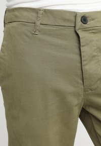 Chinos verde oliva con design a vita piatta, con chiusura a bottone e tasche visibili. Realizzati in un tessuto liscio e resistente.