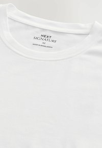 Hvid T-shirt med rund hals, der viser det trykte mærke "NEXT SIGNATURE M" og "Made in Bangladesh" indvendig i kraven.