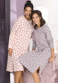 Two women in long-sleeve nightgowns: one is light pink with dark pink heart patterns, the other is gray with light pink hearts. Both have relaxed fits.